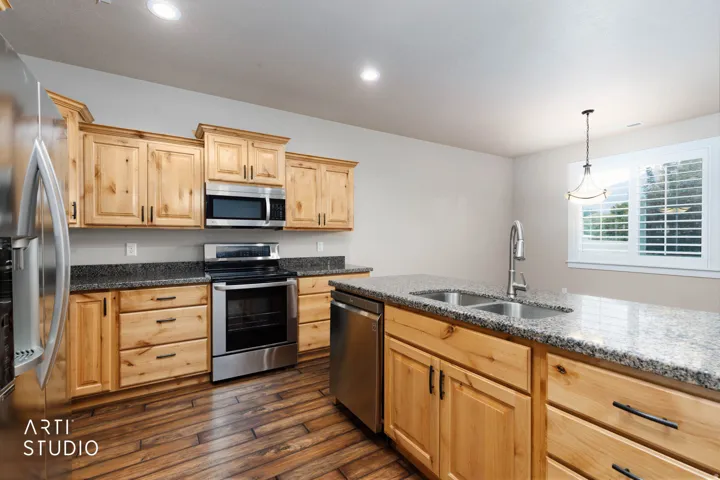 Kitchen featuring wood-finish cabinetry, stainless steel appliances, granite countertops, an island with a double basin sink, and wood-finish flooring