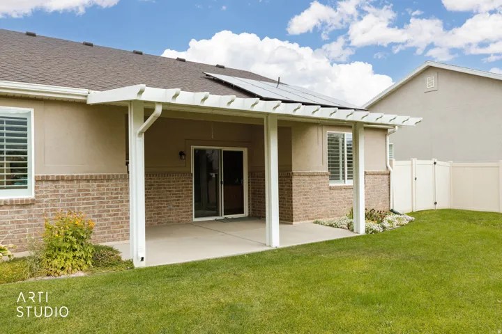 Exterior featuring a concrete patio, white pergola, sliding glass door, and solar panels