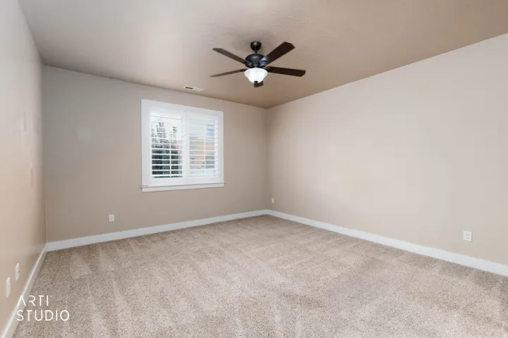 Plush carpeting, neutral wall tones, window with plantation shutters, ceiling fan with integrated lighting