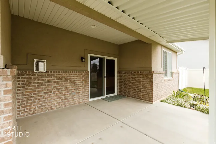 Covered patio featuring concrete flooring, brick wainscoting, stucco exterior, and sliding glass doors