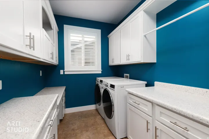 White shaker cabinetry, light speckled countertops, built-in shelf, and window with plantation shutters