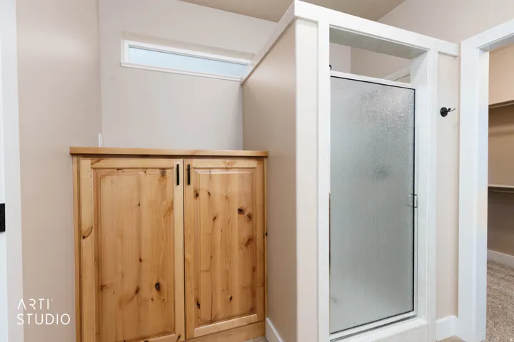 Frosted glass shower enclosure, wood-finish cabinetry with black hardware, and an upper transom window