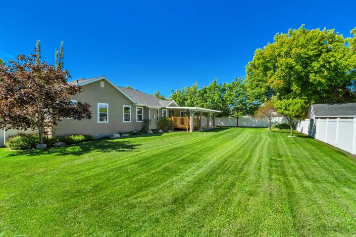 Expansive backyard featuring a manicured lawn, established trees, and a covered deck