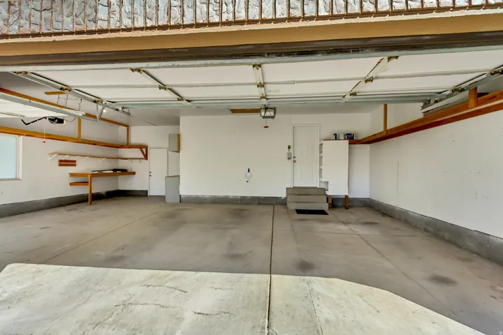 Spacious garage with exposed beam ceiling, built-in wooden shelving, and concrete flooring
