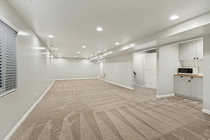 Spacious room featuring neutral carpeting, recessed lighting, a window with horizontal blinds, and a built-in cabinet with a wood-finish countertop