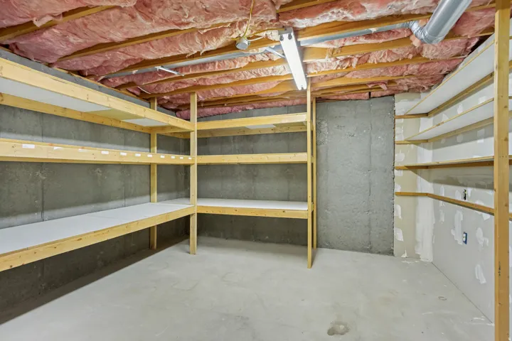Unfinished basement featuring exposed insulation, concrete flooring, and extensive built-in wooden shelving