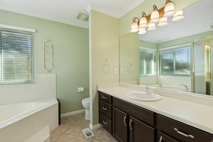 White tiled soaking tub, an expansive vanity with double sinks, dark wood-finish cabinetry, and a large wall-mounted mirror