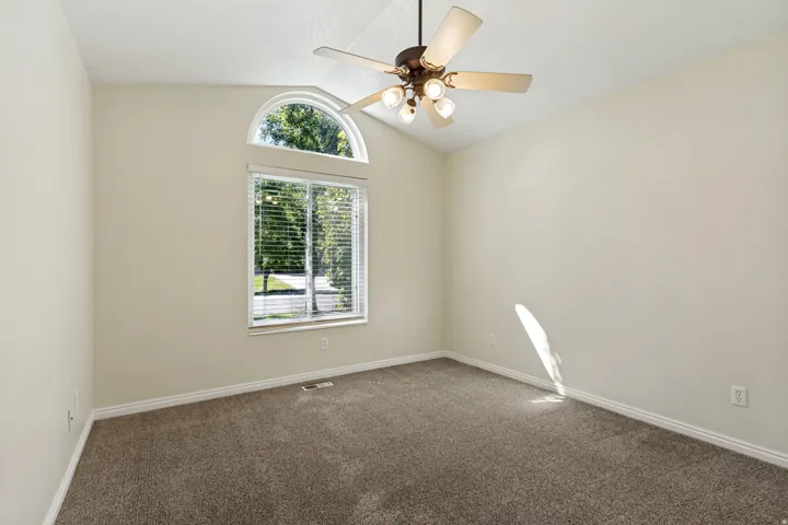 Vaulted ceiling with an arched window above a rectangular window, equipped with a ceiling fan with integrated lighting