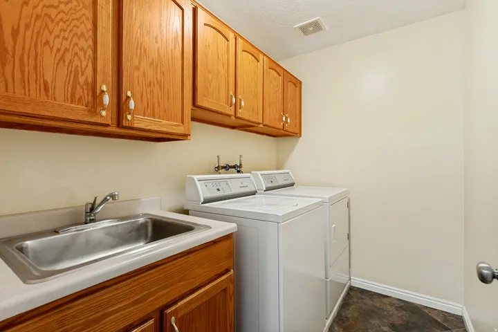 Upper and lower wood cabinets, stainless steel utility sink, neutral countertops, and dark floor tiling