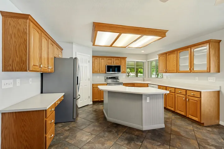 Wood-finish cabinetry, light-toned countertops, and a central island with beadboard paneling