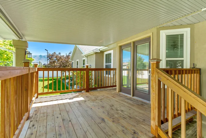 Covered wood-plank deck with wood railings, double glass-paneled doors, and a distant mountain backdrop