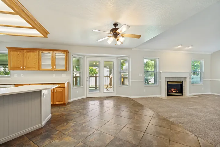 Tile flooring, a built-in fireplace, natural wood cabinetry, a ceiling fan, and French doors leading to exterior