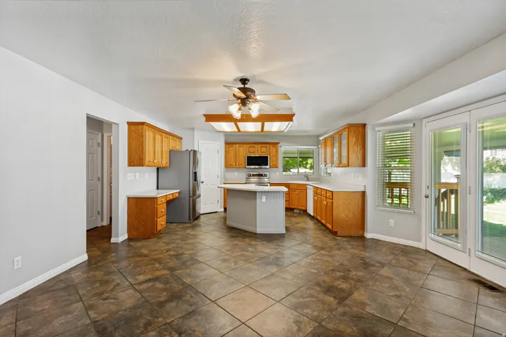 Spacious kitchen featuring warm wood cabinetry, a central island, stainless steel appliances, a white tile backsplash, and French doors