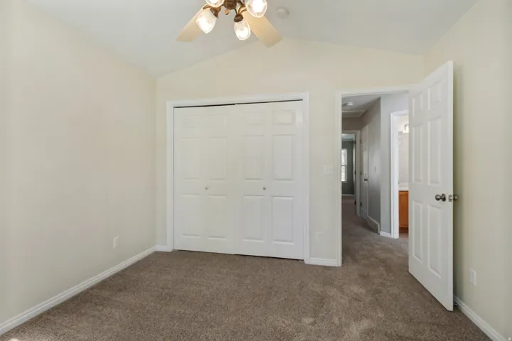 Vaulted ceiling, ceiling fan with integrated lighting, bi-fold closet doors, wall-to-wall carpeting, paneled interior doors