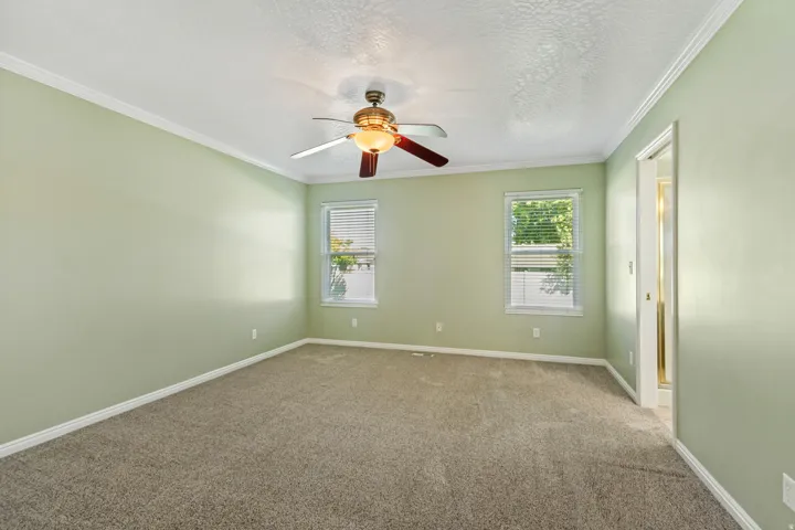 Carpeted room featuring a ceiling fan with integrated lighting, two windows with blinds, and white trim molding