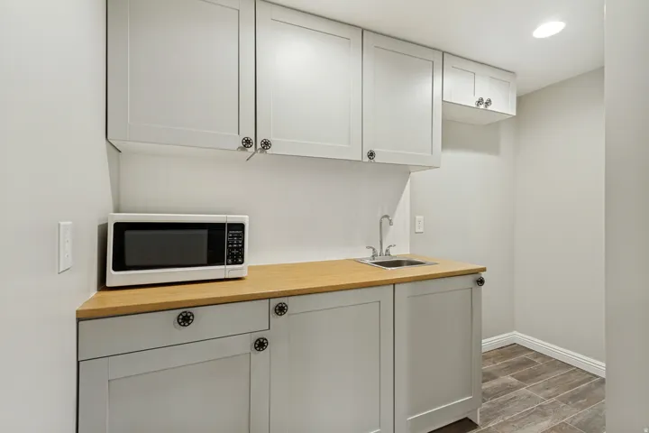 Full-height cabinetry with decorative hardware, wood-finish countertop, stainless steel sink, and wood-look flooring