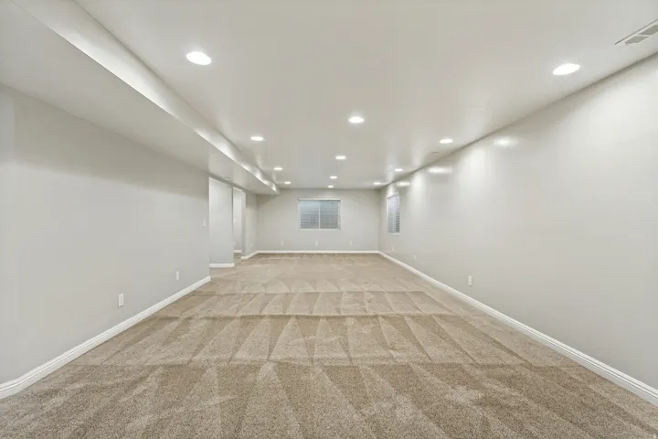 Spacious room with recessed lighting, light-colored walls, patterned carpeting, and windows with horizontal blinds