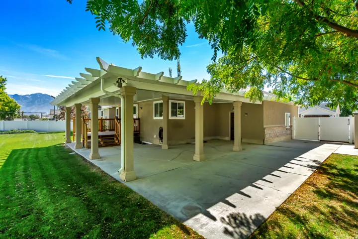 Rear exterior featuring a covered patio with pergola, stucco finish, stone veneer accent, and a privacy fence