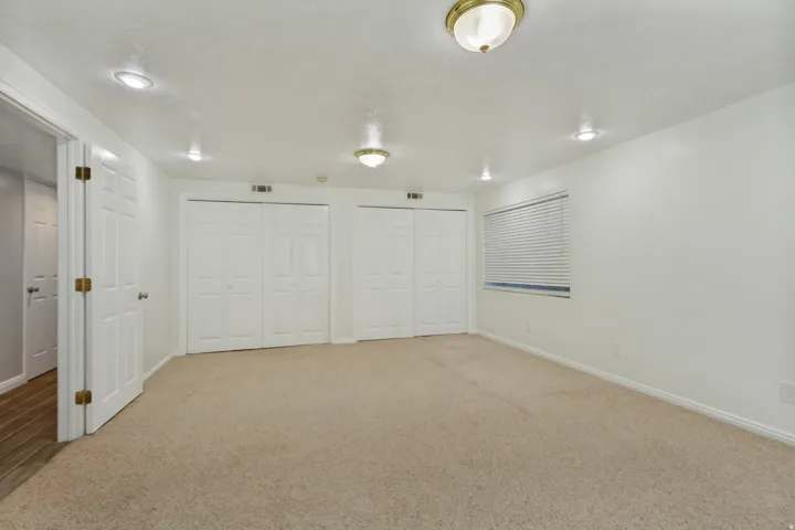 Neutral-toned carpeting, white walls, two sets of bi-fold closet doors, recessed ceiling lighting, and a window with horizontal blinds