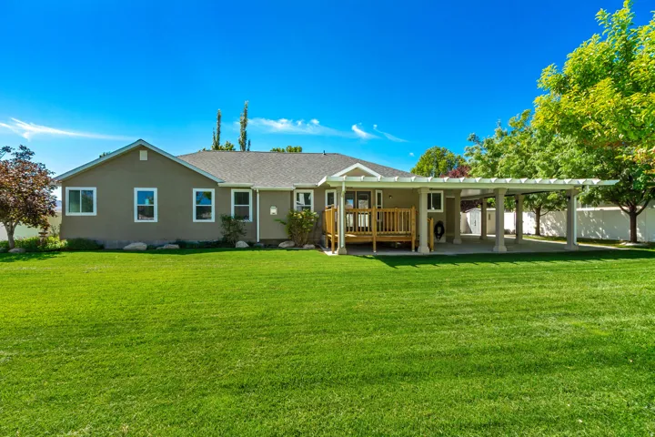 Expansive green lawn, covered patio, wooden deck, stucco exterior, and mature trees