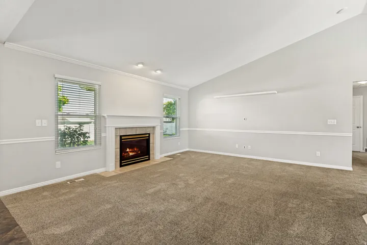 Carpeted living space featuring a fireplace with a tile surround, two windows with blinds, recessed lighting, and crown molding