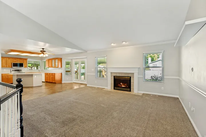 Vaulted ceiling, gas fireplace with tile surround, wood-finish cabinetry, stainless steel appliances, and double glass doors