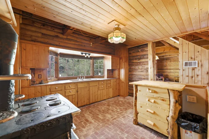 Wood-paneled kitchen featuring a bay window, wood cabinetry, a built-in sink, and brick-patterned flooring