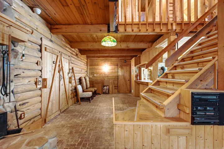Expansive interior featuring exposed log walls, a natural wood staircase, wood-plank ceilings, and brick-patterned flooring