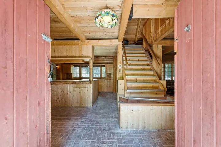 Interior featuring exposed wood beams, wood paneling, a wooden staircase, and brick-patterned flooring