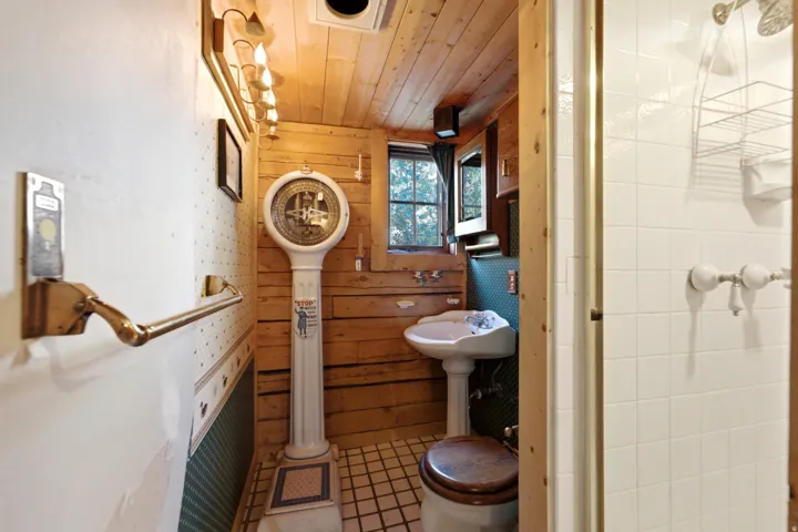 Wood-paneled bathroom featuring a pedestal sink, window, and wall-mounted lighting