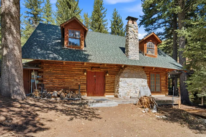 Log cabin exterior featuring a stone chimney, dormer windows, and a green shingle roof
