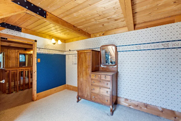 Exposed wood beam ceiling, wood plank ceiling, wood-paneled walls, carpet flooring, wall-mounted light fixture