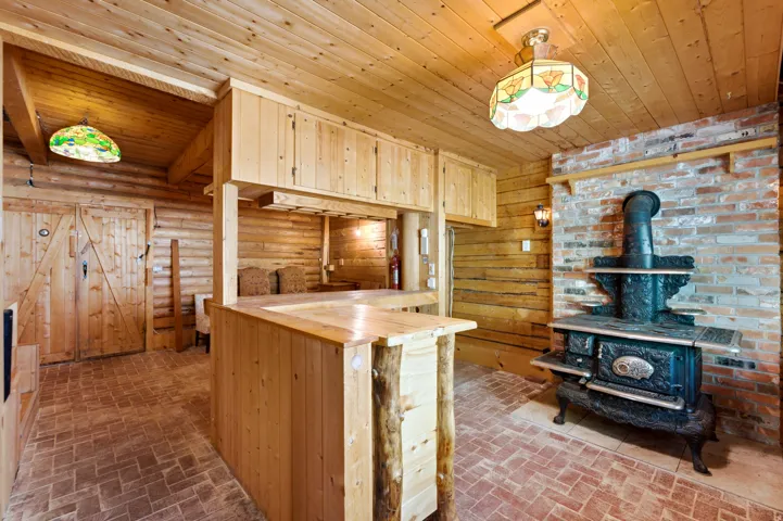 Wood-paneled walls and ceiling, brick flooring, built-in wooden bar with integrated cabinetry, and an ornate cast iron stove