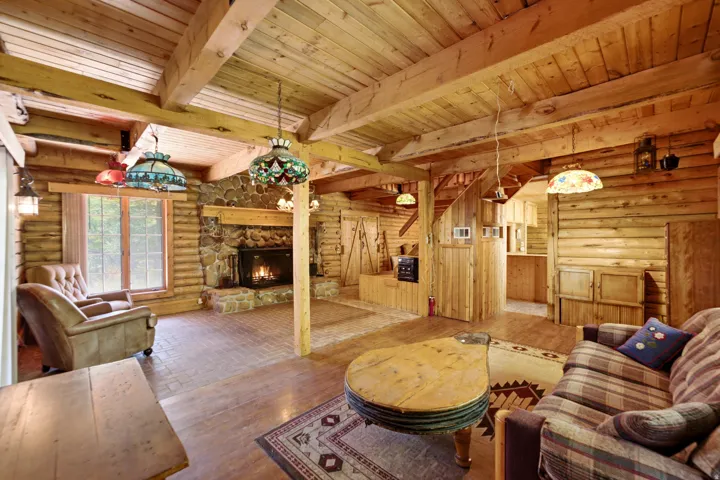 Wood-paneled walls and ceilings with exposed wood beams, stone fireplace with a wood mantle, wood-finish flooring, and recessed built-in shelving