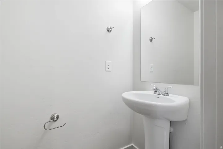 White pedestal sink with a chrome faucet, illuminated by a rectangular wall-mounted mirror