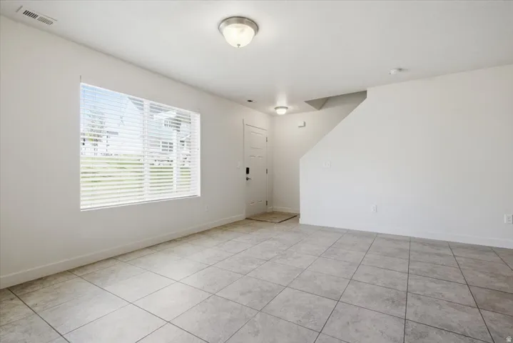 Tiled flooring, white walls, flush mount lighting, prominent window, and a staircase