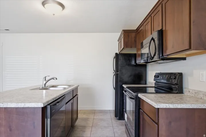 Kitchen featuring wood-finish cabinetry, light-toned countertops, tile flooring, and black appliances including a refrigerator, range, microwave, and dishwasher