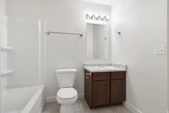 Tub/shower combination with white surround, dark wood-finish vanity, light-toned countertop, and undermount sink