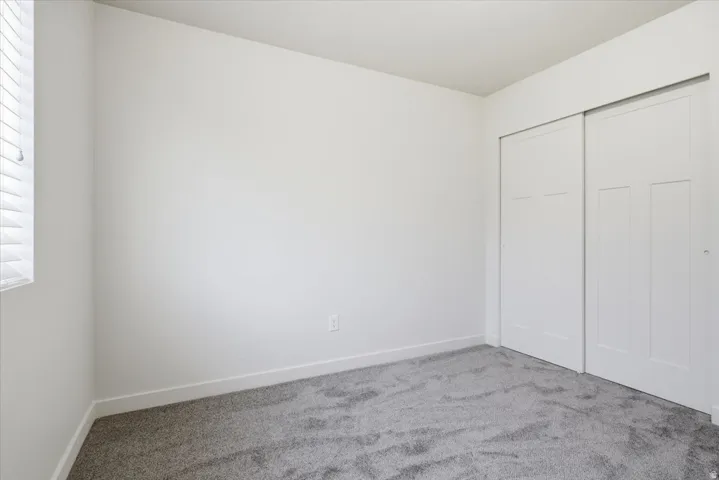 Light gray carpeting, white walls, and a window with horizontal blinds