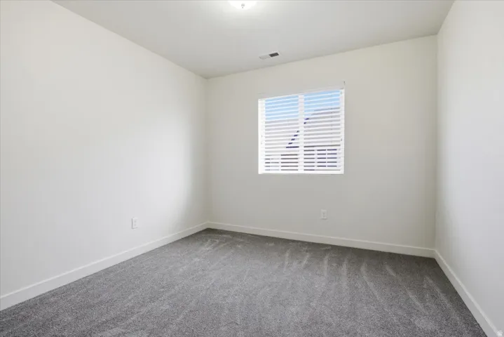 Neutral gray walls with a single window featuring horizontal blinds and a gray carpeted floor