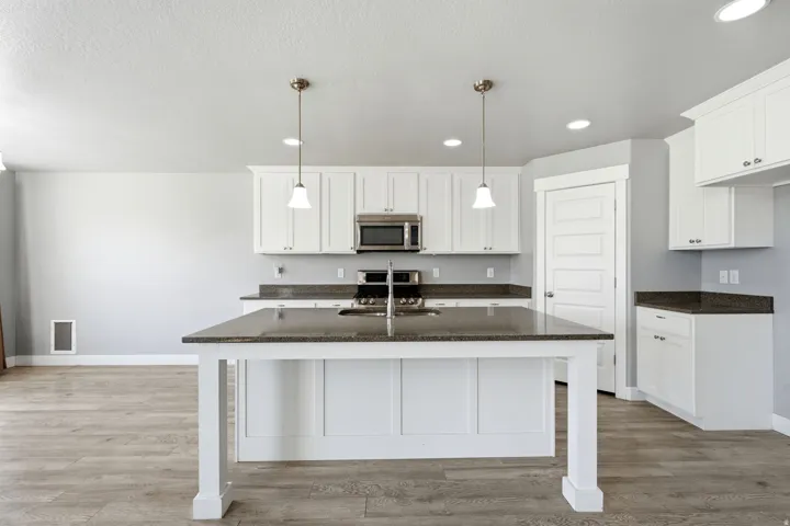 Kitchen featuring a central island, stainless steel appliances, white cabinetry, dark countertops, and recessed lighting