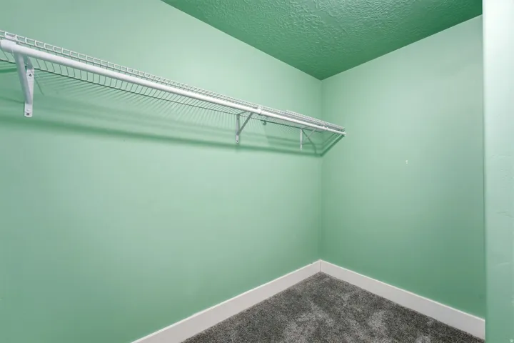 Wall-mounted wire shelving with white brackets, textured walls, and dark gray carpet flooring