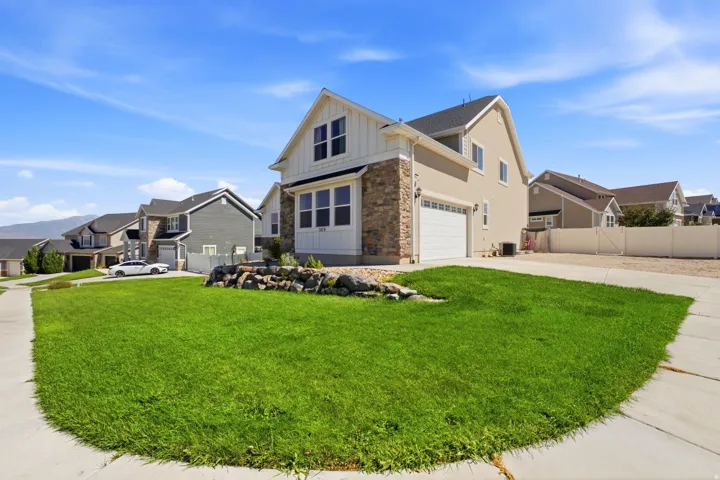 Two-story exterior with stone and siding accents, an attached garage, a paved driveway, and a front lawn with rock landscaping