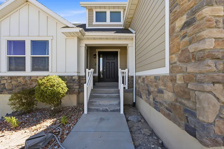 Stone and siding exterior with a covered entry, concrete steps, and a dark entry door with frosted glass