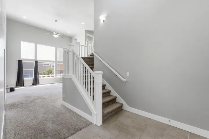 Two-story foyer with tile flooring leading to carpeted stairs with white balusters