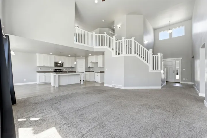 Open-concept living space featuring a two-story entryway, white kitchen cabinetry with stainless steel appliances, a kitchen island, and a dual-level staircase with white balusters