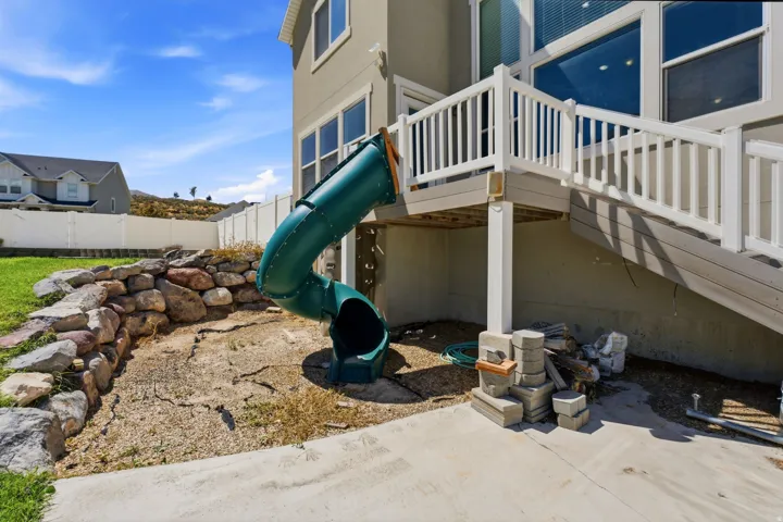 Rear exterior featuring a multi-level deck, white railing, ground-level concrete patio, and a stone retaining wall