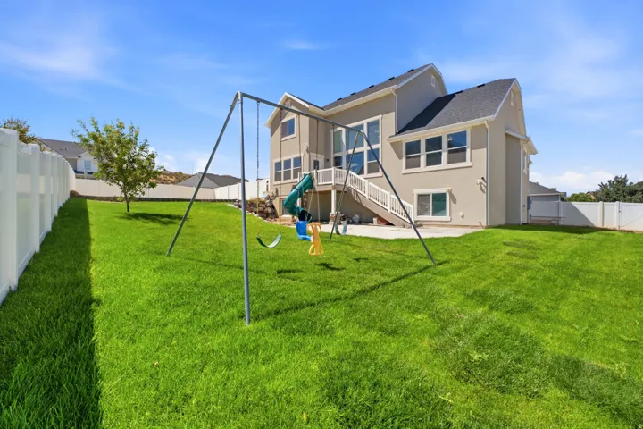 Expansive grassy yard with full fencing, a concrete patio, and a multi-story stucco exterior