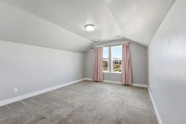 Carpeted room featuring a vaulted ceiling with an overhead light fixture, light gray wall paint, and a double window