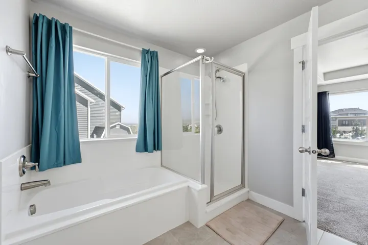 Built-in bathtub with brushed nickel fixtures, glass-enclosed shower, light-colored tile flooring, and a large window